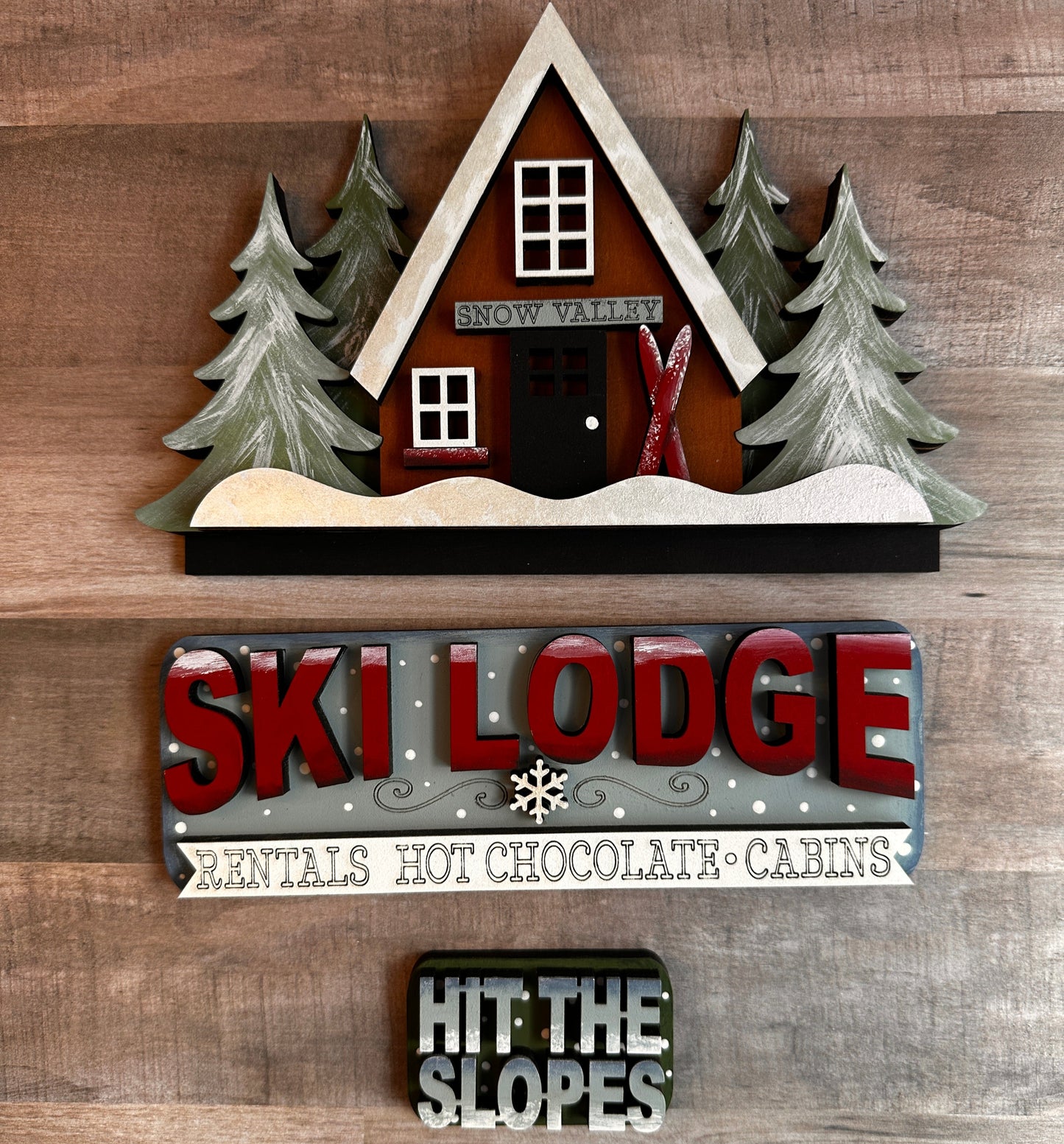 This is our Ski Lodge insert that goes with our Vintage Truck. It shows a cute A-frame ski chalet with snow-covered pine trees and skis that slides into the back of the truck's rails. The tailgate reads “Ski Lodge with a banner underneath that reads Rentals Hot Chocolate Cabins,” and the license plate reads “Hit the Slopes.” These items include Velcro dots, allowing them to adhere to the Velcro on the truck base. All these items are hand-painted with love.