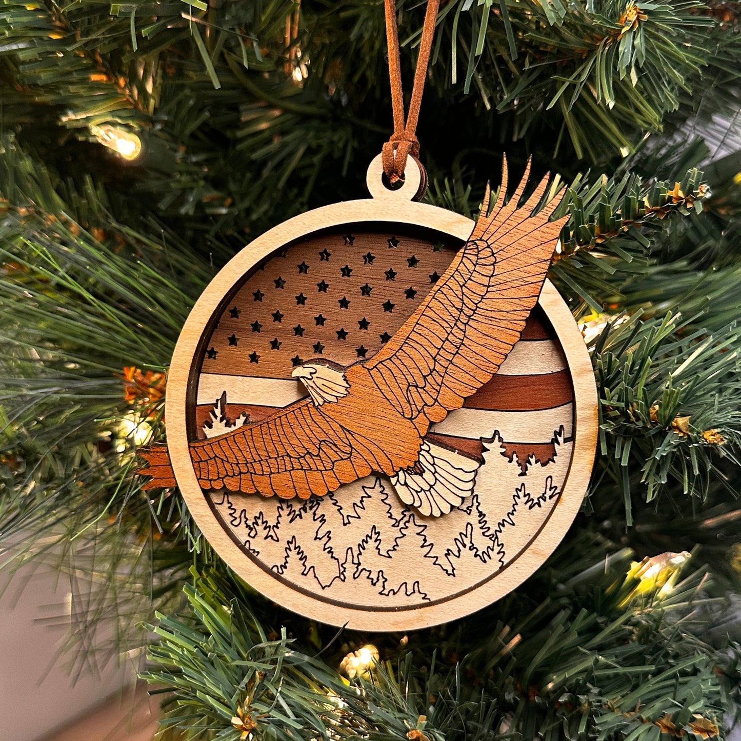 Layered wooden  eagle flying over the trees with an American flag in the back ornament made with multiple species of wood. 
