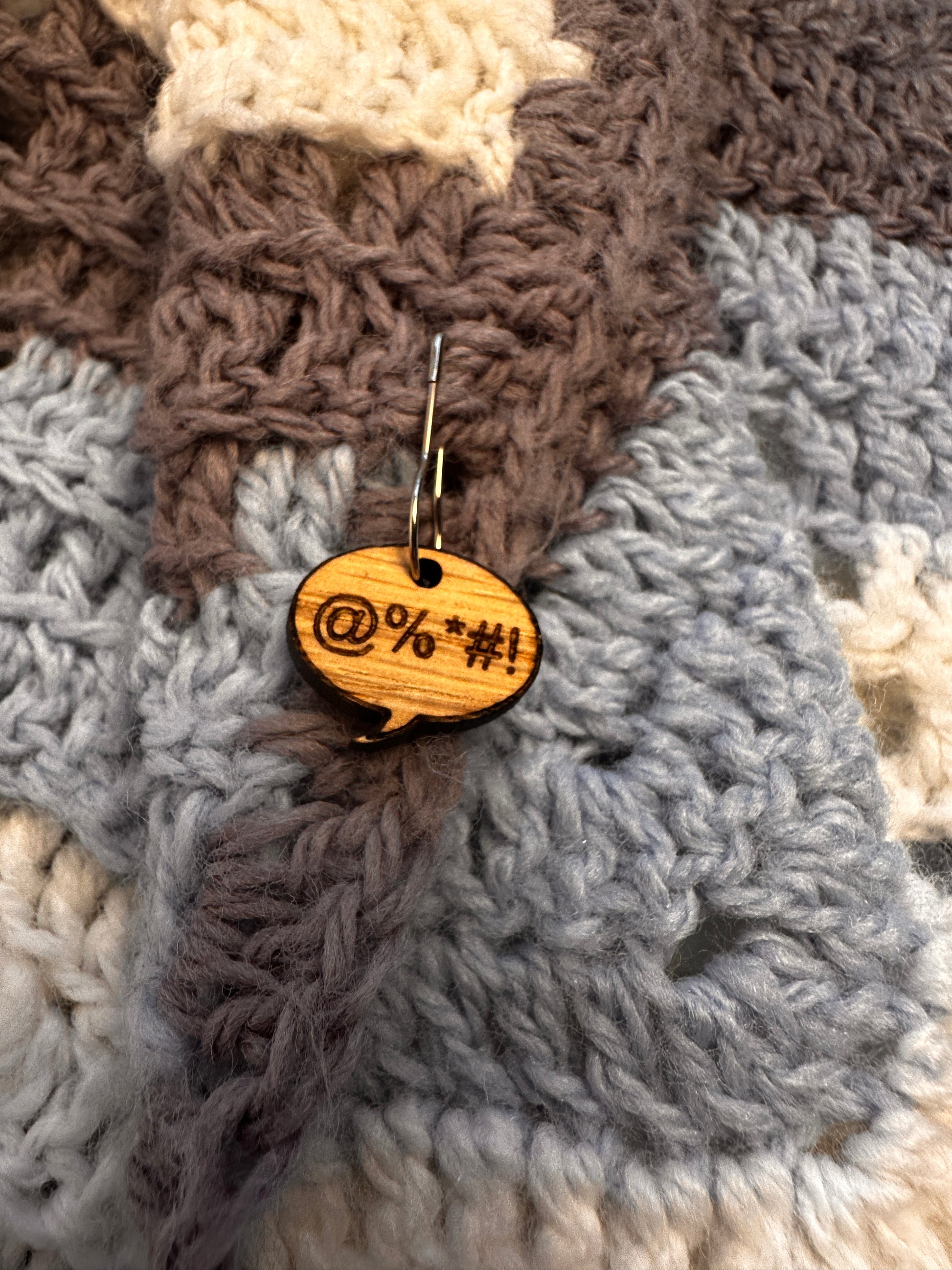 Wooden oops stitch marker engraved with an expletive, pinned to a crochet blanket. 