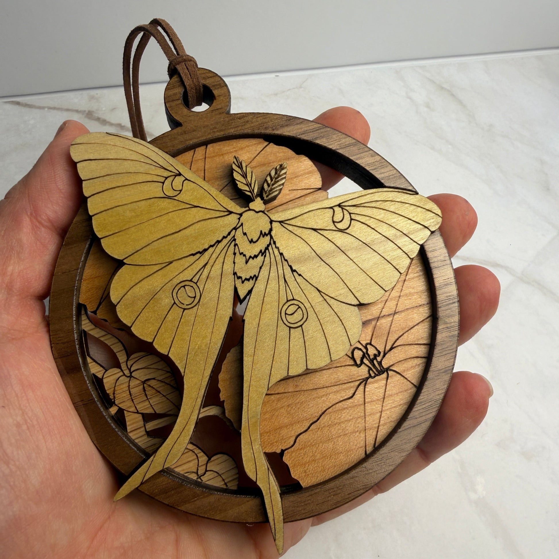 Luna moth wooden ornament being held in a hand to show the size. Made from four layers of wood: Oak, Cherry, Walnut & Poplar. 