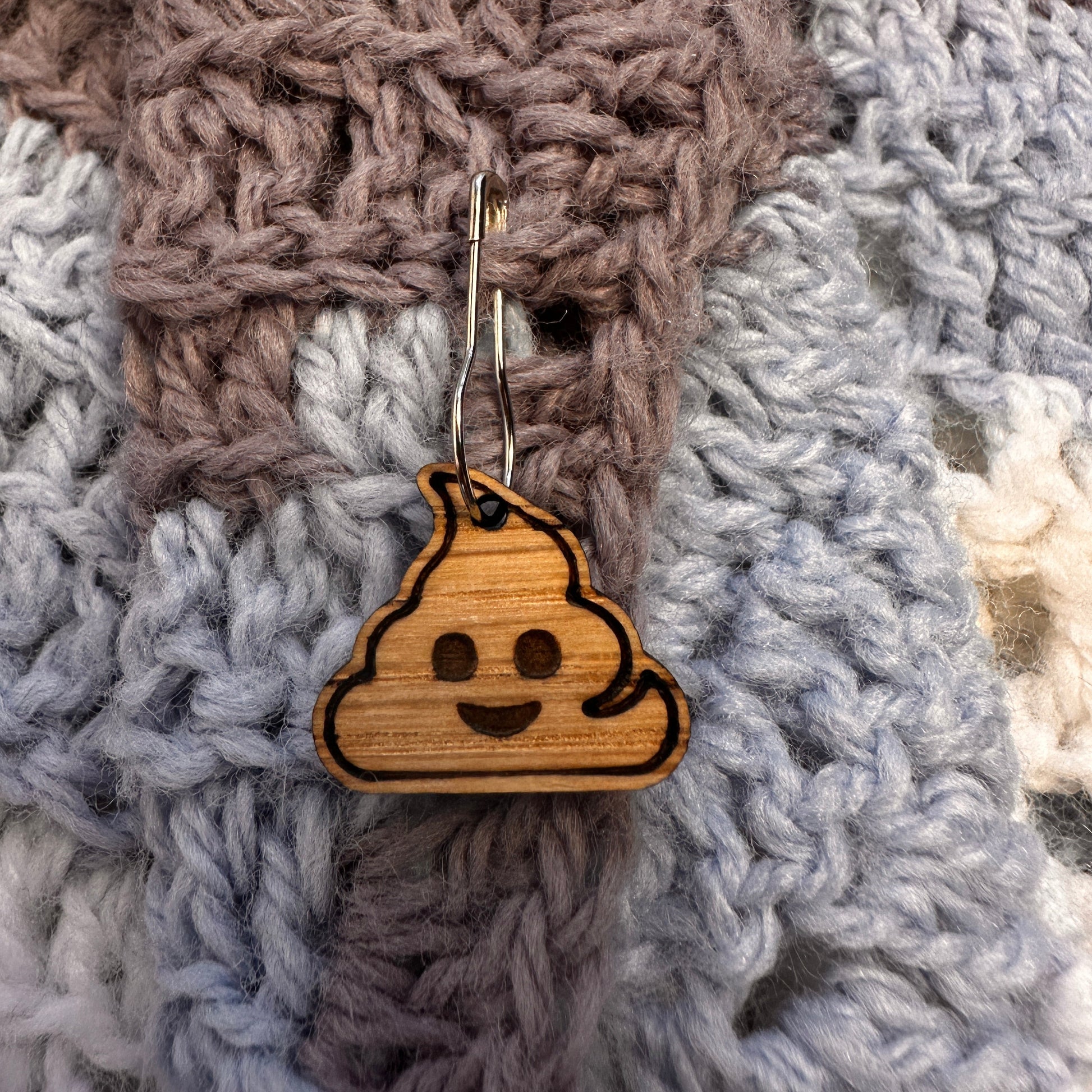 Wooden oops stitch marker in the shape of a poop emoji pinned to a crocheted blanket. 