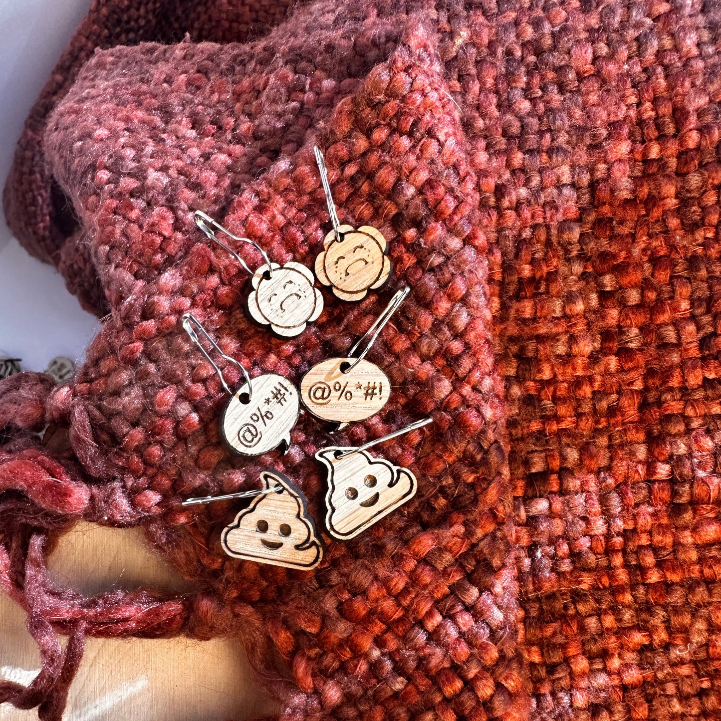 Set of OOPS stitch markers on a knitted orange and rust blanket.