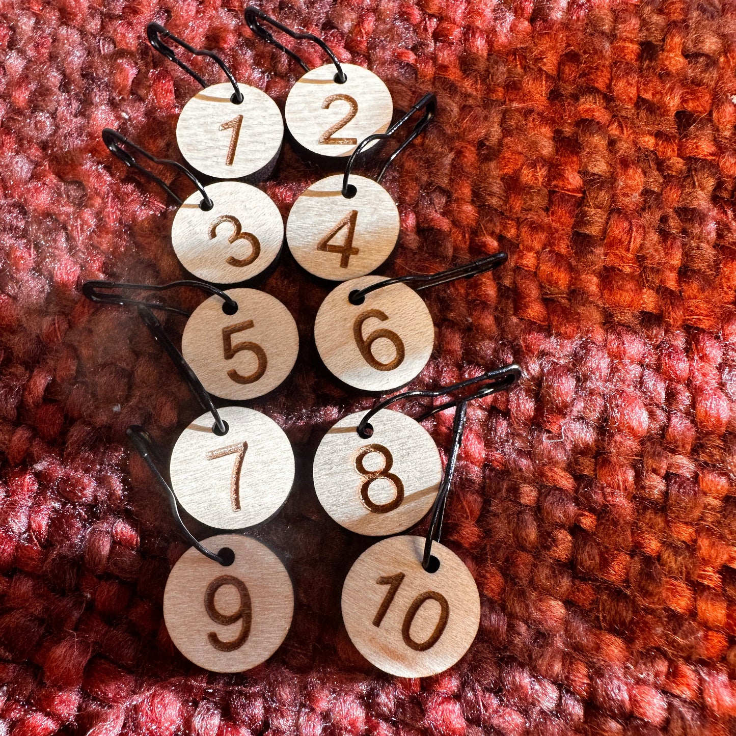 Wooden stitch markers for rows 1-10 pinned to an orange and rust blanket. 