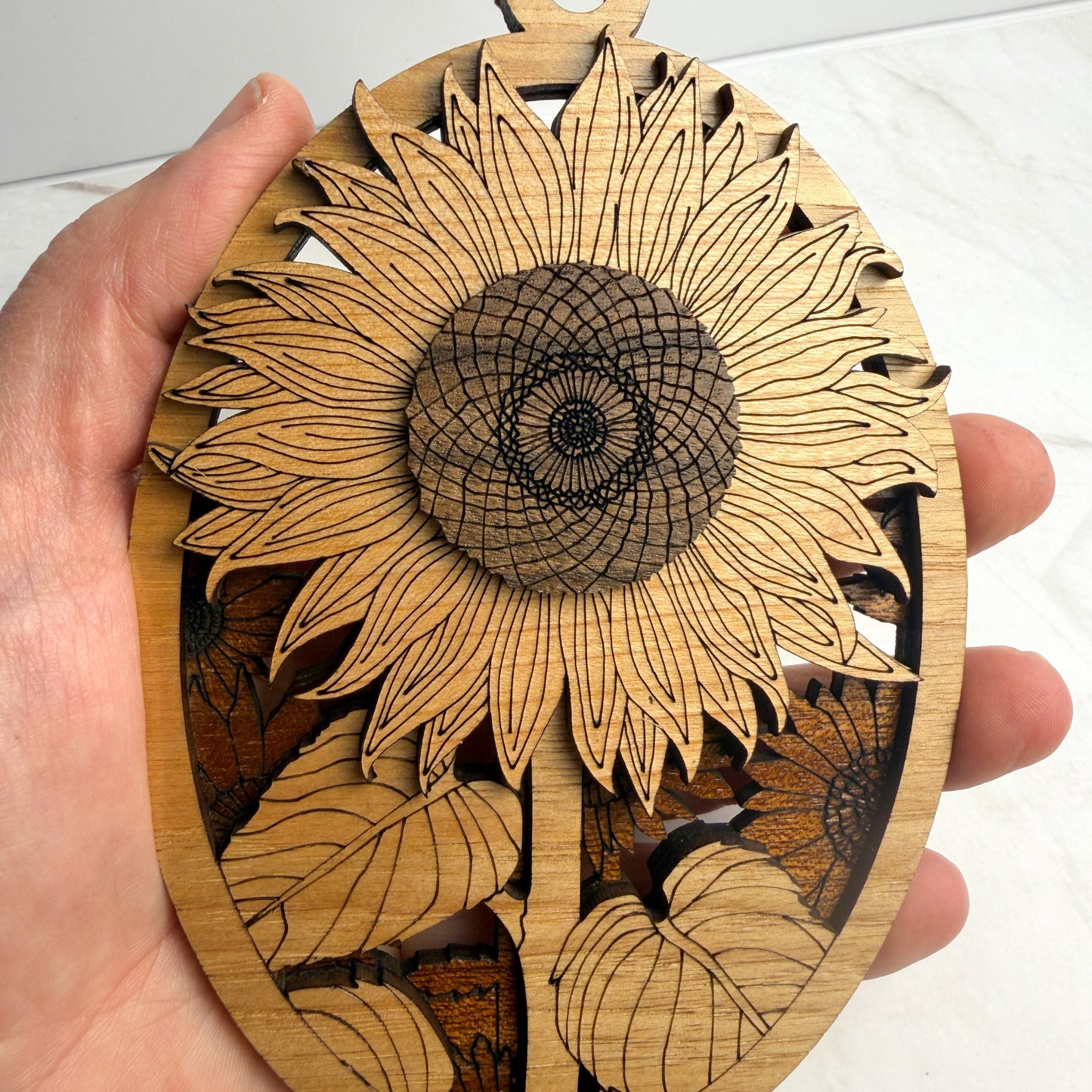 Wooden ornament with sunflower design held by a hand against a white background