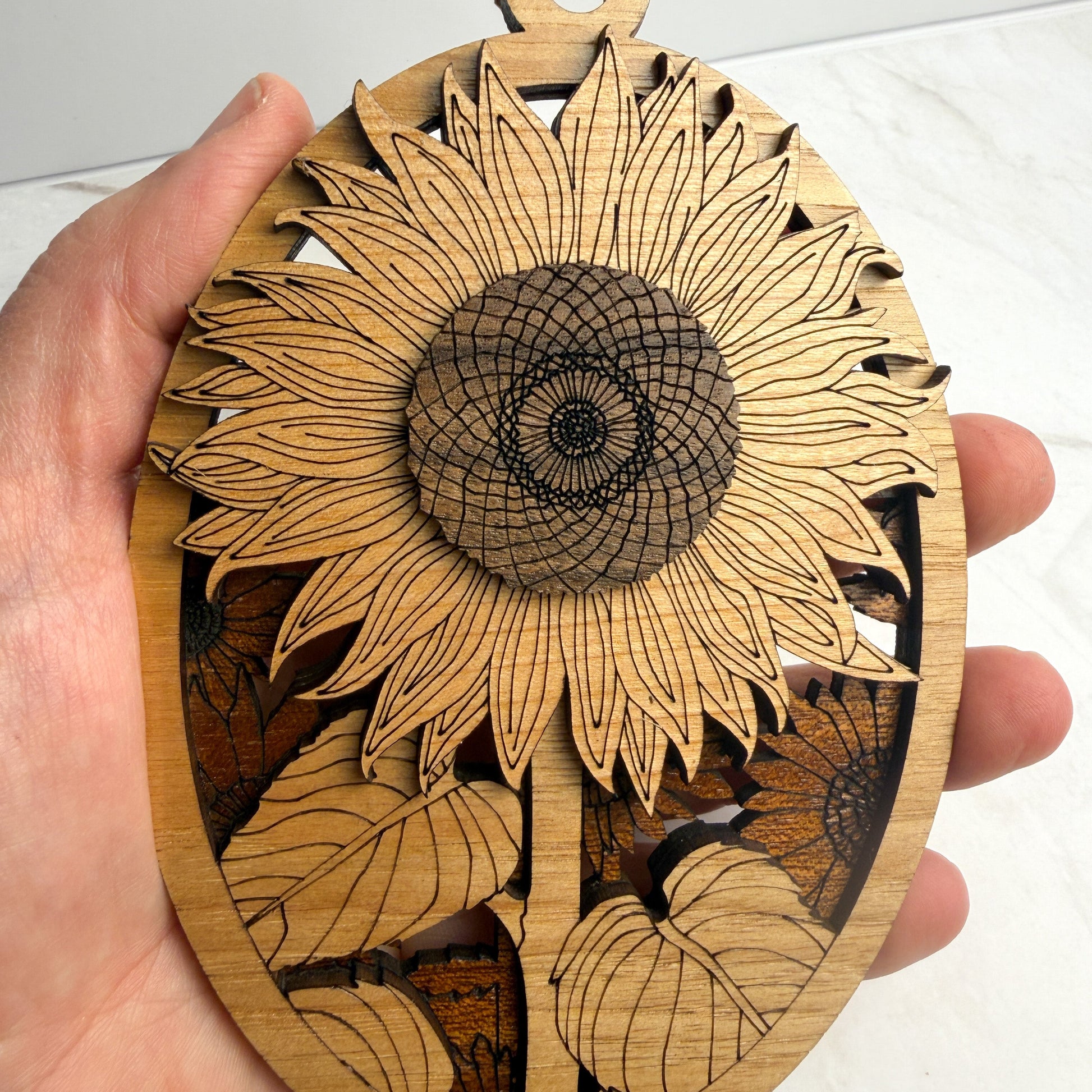 Wooden ornament with sunflower design held by a hand against a white background