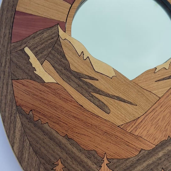 Video of a wood art piece with mountains and the sun.
